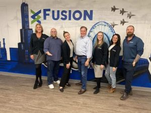 Happy people standing in front of the Fusion logo