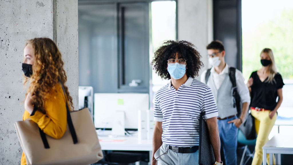 Young people with face masks back at work in office after coronavirus quarantine and lockdown, walking. - Fusion Risk Management