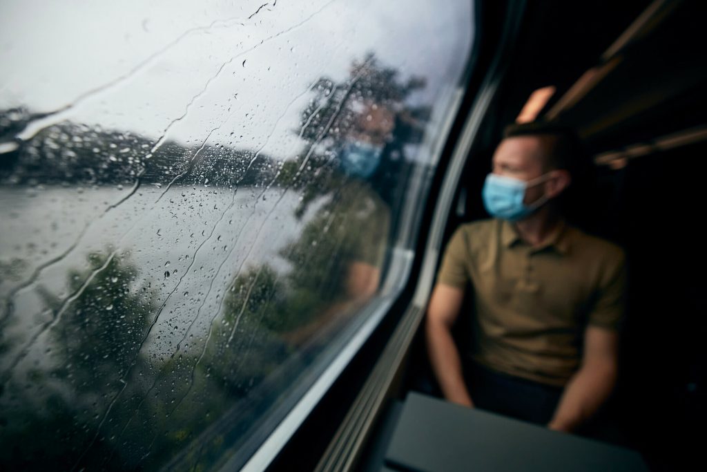 Man wearing face mask inside train in rainy day. Selective focus on raindrops on window. - Fusion Risk Management