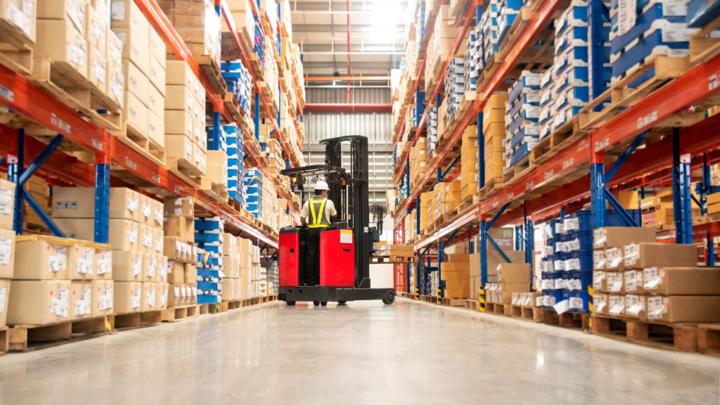 Worker in forklift-truck loading packed goods in huge distribution warehouse with high shelves. - Fusion Risk Management