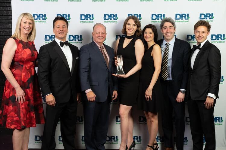 Fancy people standing in front of the DRI award wall